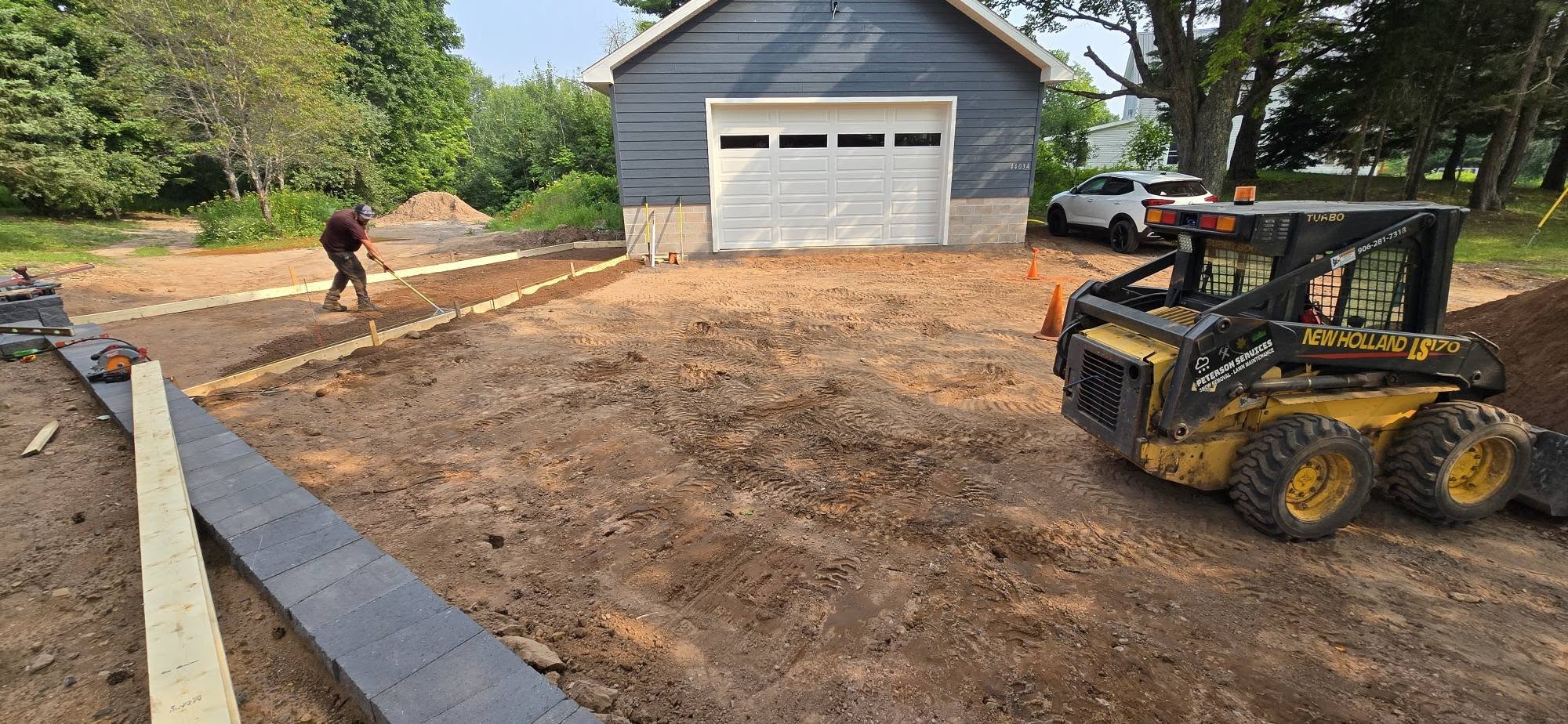 Skid steer beside a garage while retaining blocks and a new approach area are being prepared.